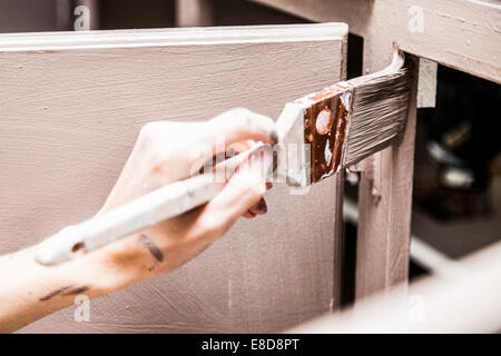 Primo piano della persona in possesso di Spazzola di vernice e verniciatura di mobili da cucina Foto Stock