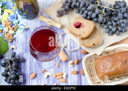 Bicchiere di vino rosso sul tavolo con uve, pane, dadi, cavatappi e tappo. Foto Stock