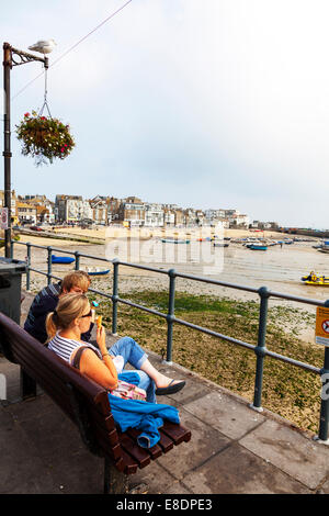 Mangiare il gelato guardando fuori St Ives Harbour Town Cornwall Regno Unito giovane seduto su un banco di lavoro rivolta verso il porto Foto Stock