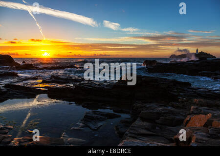Faro di Godrevy al tramonto marea onde si infrangono contro gli scogli rocciosa costa robusto litorale costiero giallo crepuscolo glow sun Foto Stock