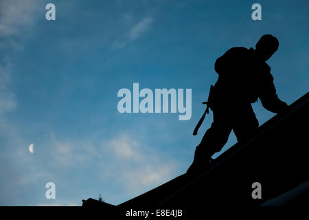 Il contraente in Silhouette lavorando su un tetto con un cielo blu in background Foto Stock