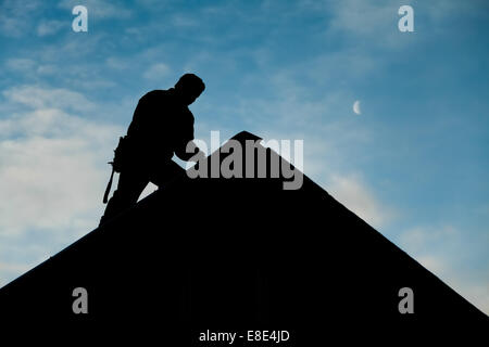 Il contraente in Silhouette lavorando su un tetto con un cielo blu in background Foto Stock