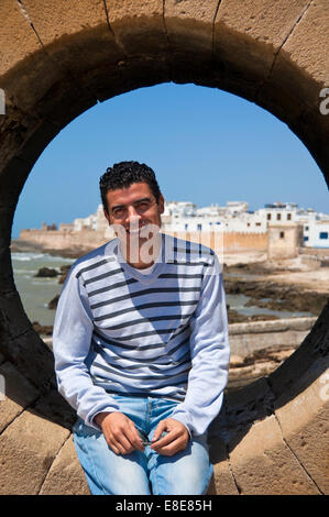 Ritratto verticale di un locale marocchino uomo seduto in un oblò a skala a Essaouira Foto Stock