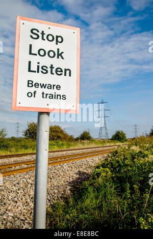 Attraversamento del piede di una trafficata linea ferroviaria con un cartello di avvertimento smettere di guardare e ascoltare per treni Foto Stock