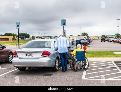 Un uomo anziano si prepara ad aiutare la sua moglie disabili nelle loro auto in un parcheggio nella città di Oklahoma, Oklahoma, Stati Uniti d'America. Foto Stock