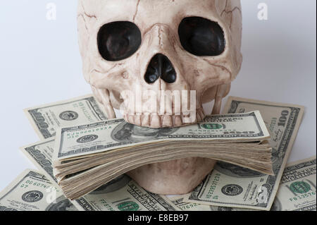 Cranio umano circondato da pile di banconote da cento dollari concetto avidità Foto Stock
