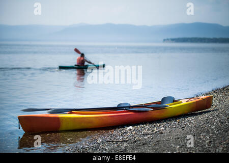 Arancio e giallo Kayak sulla riva del mare durante una bella giornata d'estate con un irriconoscibile persone fare kayak in background Foto Stock