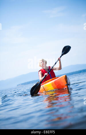 Giovane donna kayak da sola su un mare calmo e di indossare un giubbotto di sicurezza Foto Stock