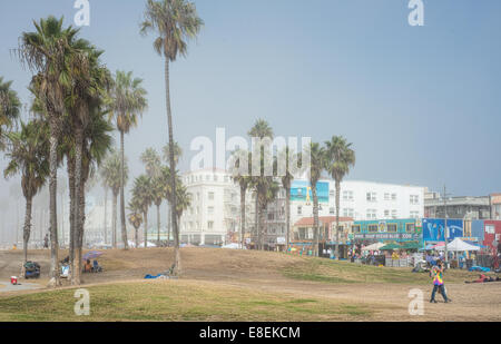 Gli amanti dello shopping a piedi lungo la spiaggia di Venice Boardwalk e gente seduta sul prato in una nebbiosa mattina Foto Stock