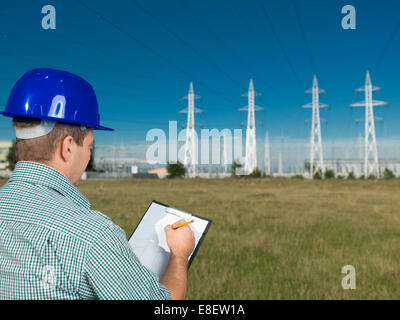 Closeup, vista posteriore del tecnico maschio sulla scrittura di appunti alla stazione elettrica Foto Stock