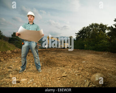 Giovane architetto caucasici in piedi sul sito in costruzione azienda cianografia Foto Stock