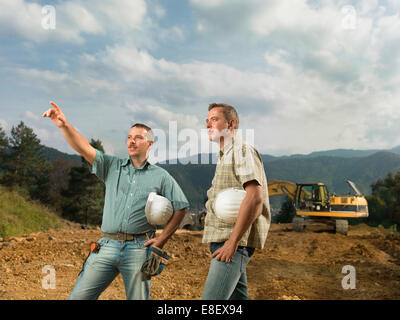 Due ingegneri caucasici in piedi, uno di loro pointingat costruzioni in corso Foto Stock