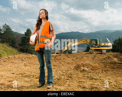 Ingegnere femmina operaio sul cantiere aperto con escavatore in background Foto Stock