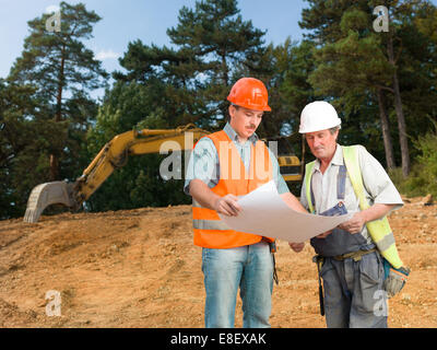 Vista frontale del manager e builder sul sito in costruzione guardando blueprint e discussione Foto Stock