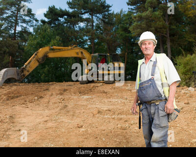 Ritratto di senior operaio in uniforme blu sul sito in costruzione all'aperto Foto Stock