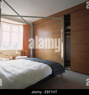 Metallo fourposter letto con piumone bianco e grigio buttare in camera da letto moderna con pannelli di legno porte su grandi guardaroba a muro Foto Stock