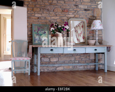 Immagine e specchio con brocca di fiori sul dipinto di blu pallido tabella esposto contro il muro di pietra nel cottage hall Foto Stock