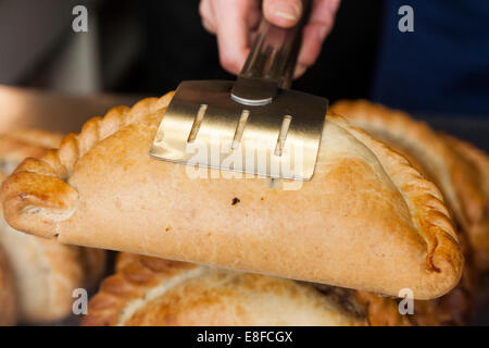 Immagine di un Cornish pasty detenute da servire le tenaglie sul display di un negozio pastoso. Mevagissey, Cornwall. Regno Unito. Foto Stock