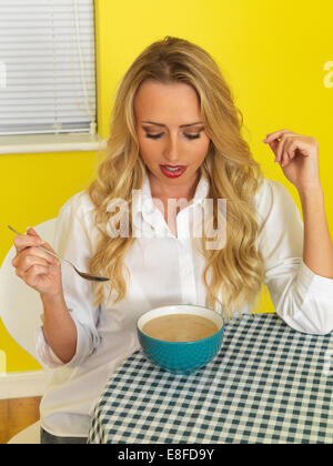 Fiducioso felice giovane donna, mangiare una tazza di acqua calda fresca zuppa nutriente, contro uno sfondo giallo Foto Stock