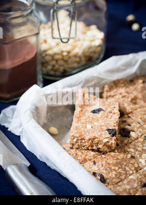 In casa fragranti granola (muesli) barre della proteina fatta di burro di arachidi, miele, noci e uvetta passa su un foglio di carta forno. Foto Stock