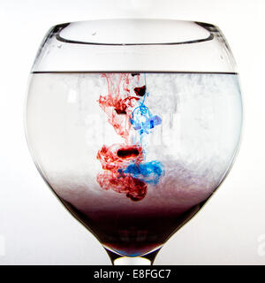 Il rosso e il blu inchiostro sciogliere in un bicchiere di acqua Foto Stock