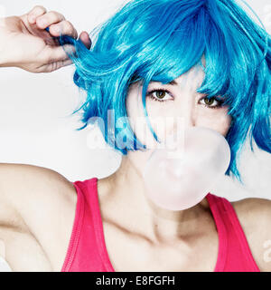 Ritratto di una donna in blu parrucca soffiando bubblegum bubble Foto Stock
