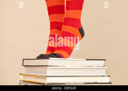 Primo piano di una donna in calze stripy in piedi sui tiptoes su una pila di libri hardback Foto Stock