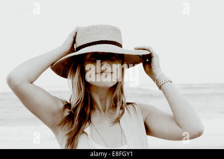 Ritratto di una donna sorridente in piedi sulla spiaggia tenendo il suo cappello, Sudafrica Foto Stock