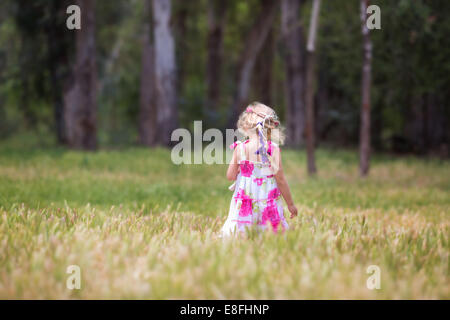 Vista posteriore di una ragazza che cammina attraverso un campo che porta un orsacchiotto, California, Stati Uniti Foto Stock