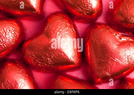 Cioccolatini a forma di cuore in lamina rossa su sfondo rosso Foto Stock