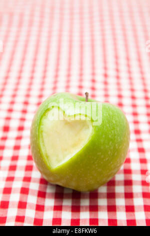 Forma del cuore mancante dal lato di una mela verde su una tovaglia spuntata Foto Stock