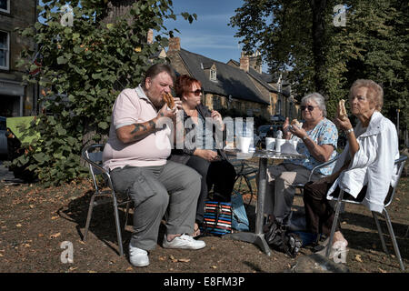 Gruppo di maturare la gente inglese tucking in malsana junk food costituito da hamburger e hot dogs in una posizione esterna. Mangiare all'aperto REGNO UNITO Foto Stock