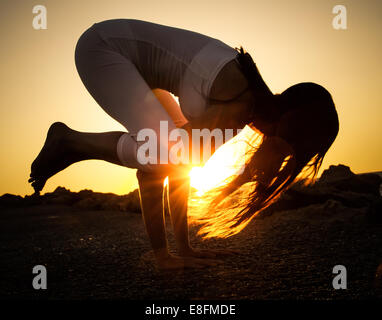 La donna a praticare yoga sulla spiaggia al tramonto Foto Stock