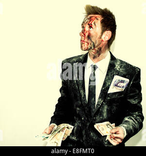 Uomo sanguinato in un vestito sporco che tiene una manciata di soldi Foto Stock