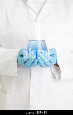 Close up di scienziato tenendo un matraccio conico di liquido di colore blu Foto Stock