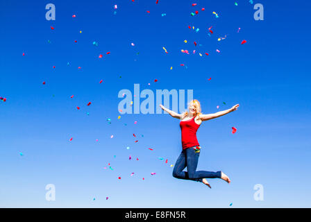 Ritratto di donna bionda jumping con i confetti contro il cielo blu Foto Stock