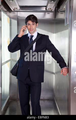 Imprenditore in un ascensore a parlare al telefono Foto Stock
