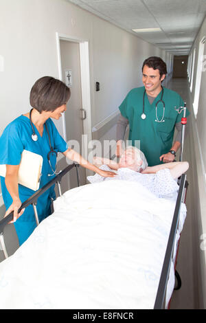 Due medici spostamento del paziente sul letto lungo il corridoio di ospedale Foto Stock