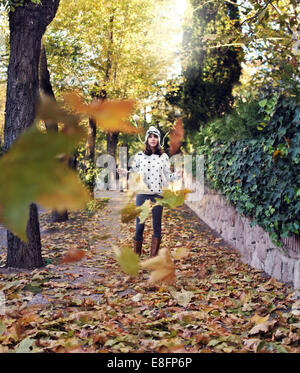 Donna in piedi gettando foglie autunnali nel parco Foto Stock