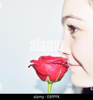 Close-up ritratto di una ragazza adolescente odorare un fiore rosa Foto Stock