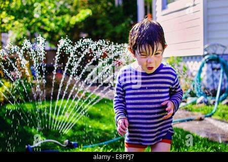 Ragazzo che corre attraverso un irrigatore da giardino, Stati Uniti Foto Stock