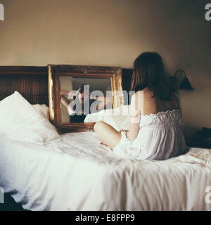 Donna seduta a letto guardando in specchio guardando il suo gridare riflessione Foto Stock
