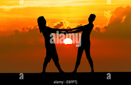 Silhouette di una giovane tenendo le mani sulla spiaggia al tramonto, Thailandia Foto Stock