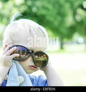Ragazzo cerca su occhiali da sole Foto Stock
