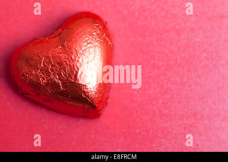 Cioccolato a forma di cuore in lamina rossa su sfondo rosso Foto Stock