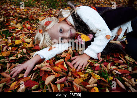 Ragazza sorridente sdraiata sull'erba tra le foglie d'autunno Foto Stock
