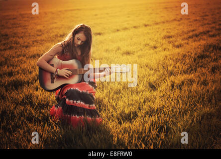 Sorridente ragazza seduta in un prato al tramonto suonando la chitarra, Polonia Foto Stock