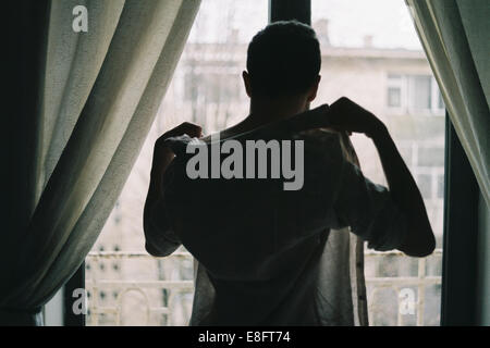 Uomo in piedi davanti a una finestra che si veste Foto Stock