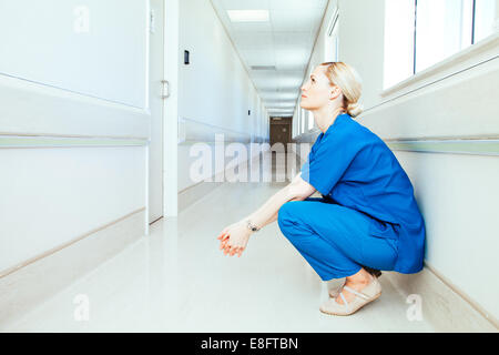 Una dottoressa stanca che si accovacciano in un corridoio di ospedale vuoto Foto Stock