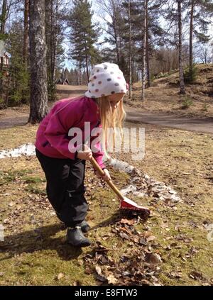 Ragazza che rastrellano foglie autunnali nel giardino, Svezia Foto Stock